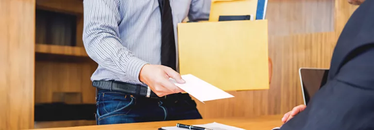 Ein Angestellter, der ein Hemd und eine Krawatte trägt, reicht seinem Chef ein Kündigungsschreiben, während er eine Schachtel mit Dokumenten hält.