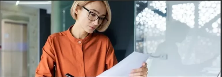 Woman with blonde hair and glasses reading a piece of paper