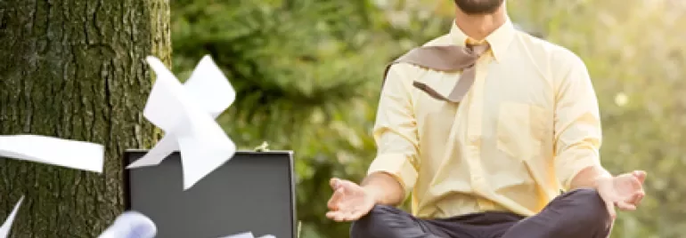 Person meditating outdoors as papers fly from a briefcase.