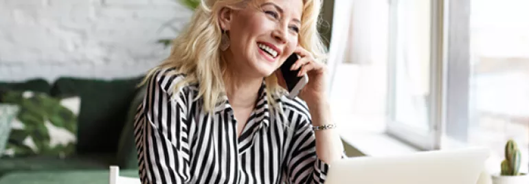 Personne souriant lors d'un appel téléphonique en utilisant un ordinateur portable.