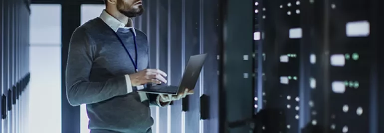 Personne dans une salle de serveurs tenant un ordinateur portable.