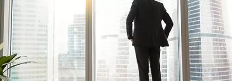 Personne en costume regarde la ville à travers de grandes fenêtres.