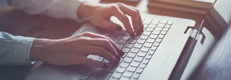 Personne tapant sur un ordinateur portable à un bureau, avec des carnets et un stylo à proximité.