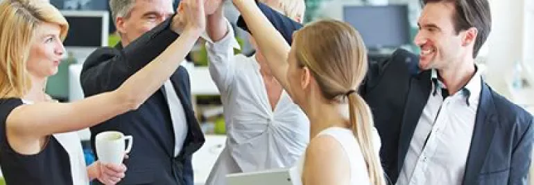 Group of colleagues celebrating with high fives in an office.
