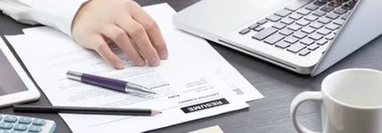 Iemand werkt op een laptop met cv-documenten op het bureau.