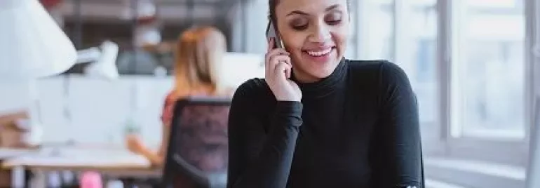 Personne en col roulé parlant au téléphone et écrivant à un bureau dans un bureau moderne.