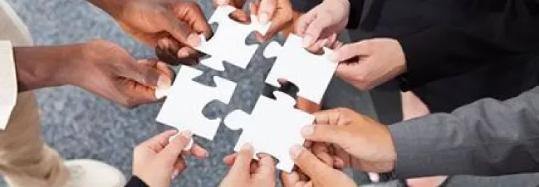 Groupe de mains assemblant des pièces de puzzle sur un fond gris.