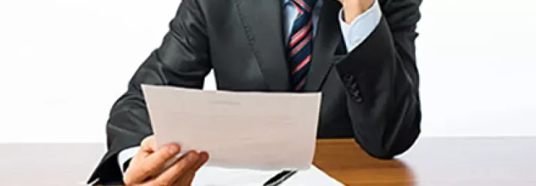 Personne en costume lisant un document à un bureau.