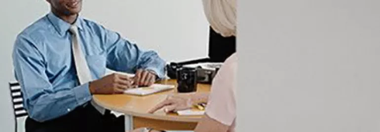 Two people having a conversation at a small table in an office setting.