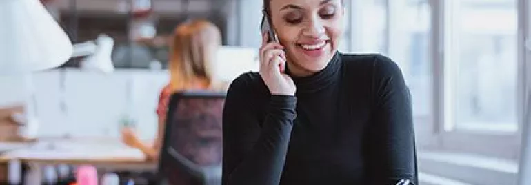 Persoon aan de telefoon en notities makend aan een bureau.