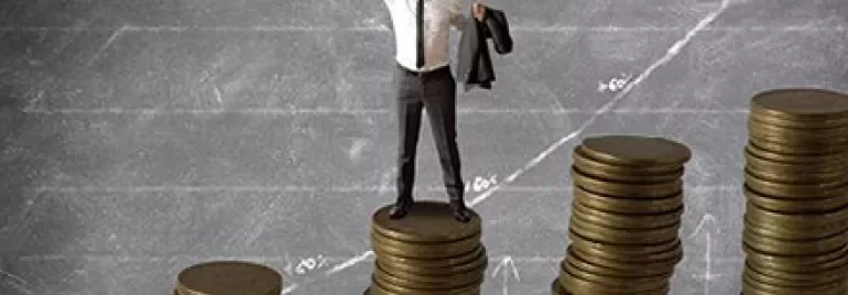 Person standing on stacks of coins with an upward graph in the background.