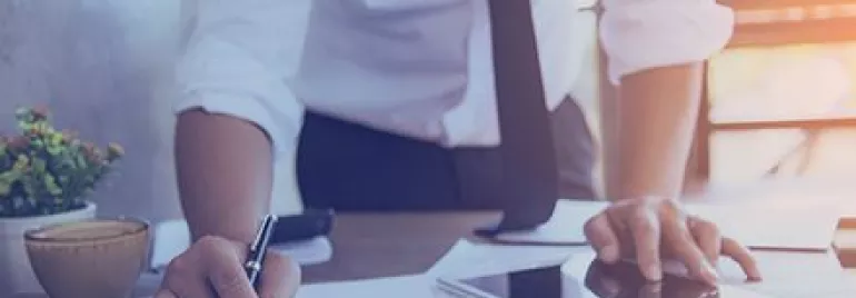 Persoon bekijkt documenten en gebruikt een tablet op een bureau.