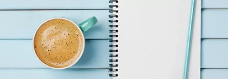 Spiraalnotitieboek met 'To Do List,' blauw potlood, en een kop koffie op een houten tafel.