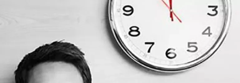 Personne avec des lunettes regardant une horloge murale.