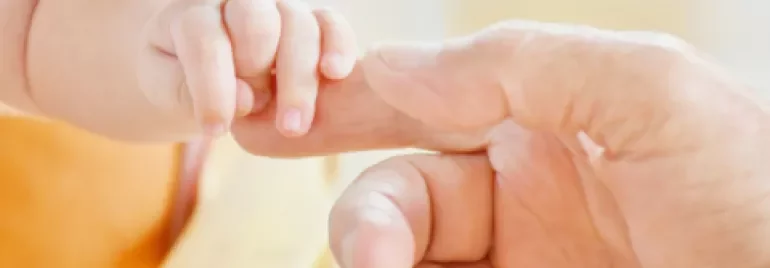 Een baby houdt de vinger van een volwassene vast.
