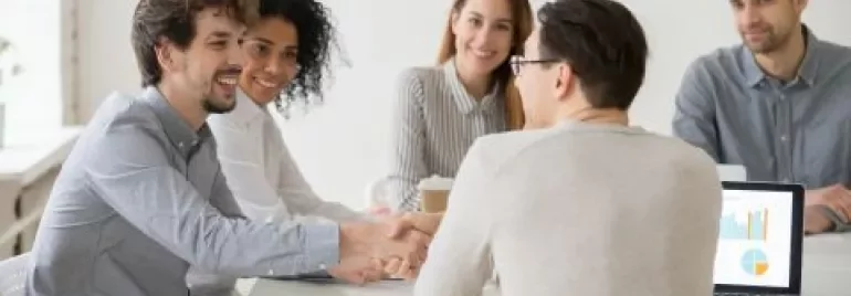 People sitting at a table having a meeting, one person shaking hands.
