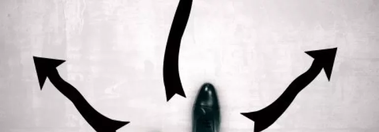 Person standing at crossroads with arrows in different directions.