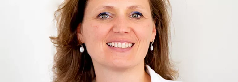 Person smiling, wearing a white jacket and earrings.