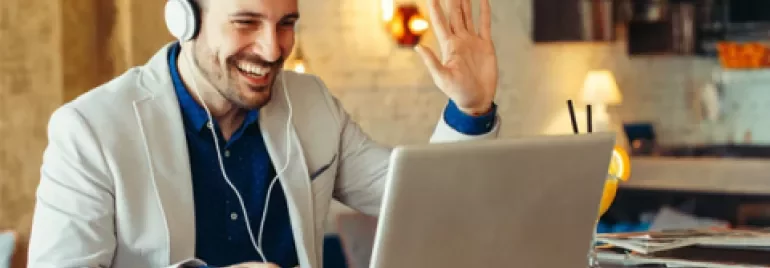 Persoon glimlacht en zwaait tijdens videobel op laptop.