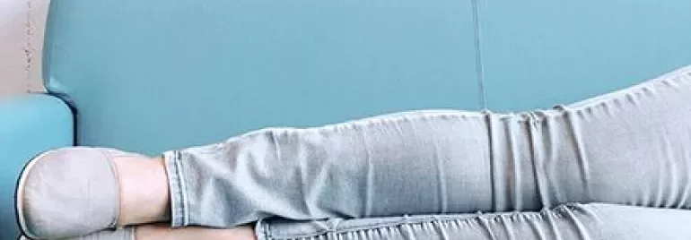 Persoon loungt op een turquoise bank, benen gestrekt in lichte jeans en slippers.