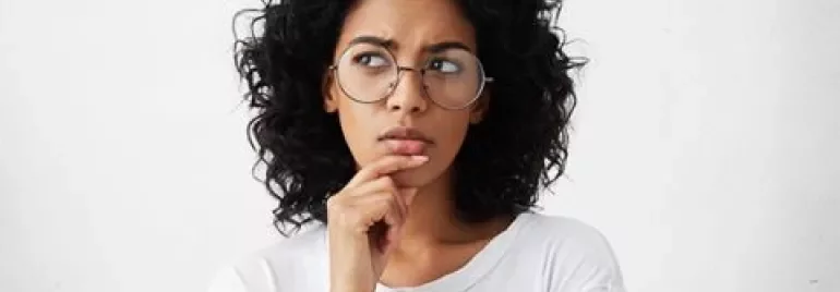 Personne aux cheveux bouclés et lunettes pensant, main sur le menton.