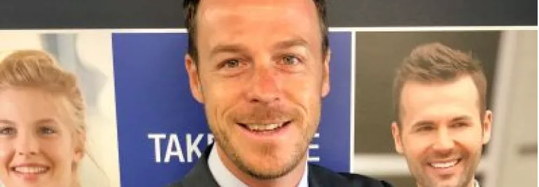 Personne souriante devant des affiches promotionnelles.
