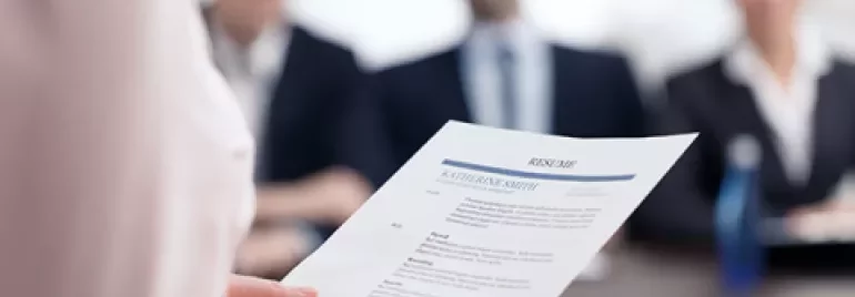 Une personne tient un CV devant un panel lors d'un entretien d'embauche.
