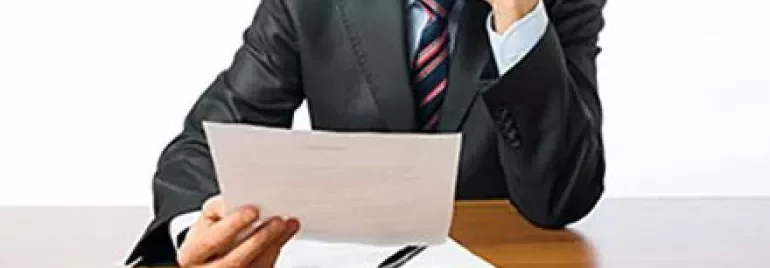Person in suit reading a paper at a desk.