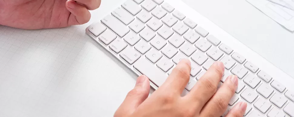 Handen typen op een wit computertoetsenbord.