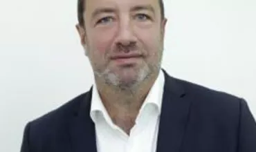 Person in a suit with a white shirt in front of a white background.