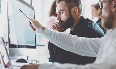 Personnes travaillant ensemble dans un bureau, regardant des écrans d'ordinateur.