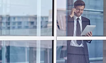 Personne en costume utilisant une tablette et parlant au téléphone près de la fenêtre.