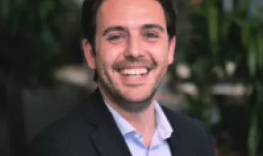 Person smiling in an office setting with plants in the background.
