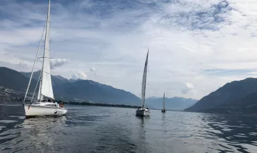 Zeilboten op een rustige meer met bergen onder een bewolkte hemel.