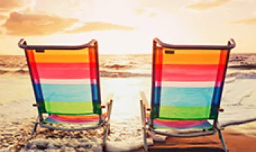Deux chaises de plage colorées face à l'océan au coucher du soleil.