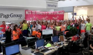Een grote groep mensen in een kantoor, juichend en met een spandoek.