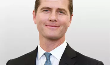 Personne en costume souriant devant un fond clair.