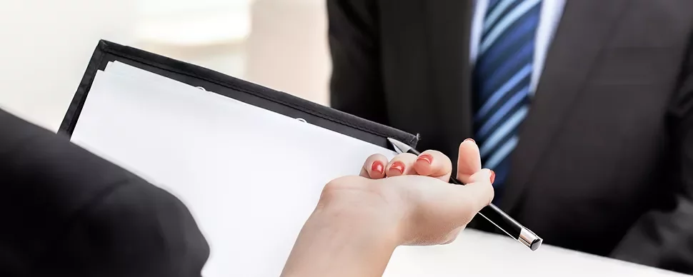 Hands holding a clipboard with a blank paper and a pen.