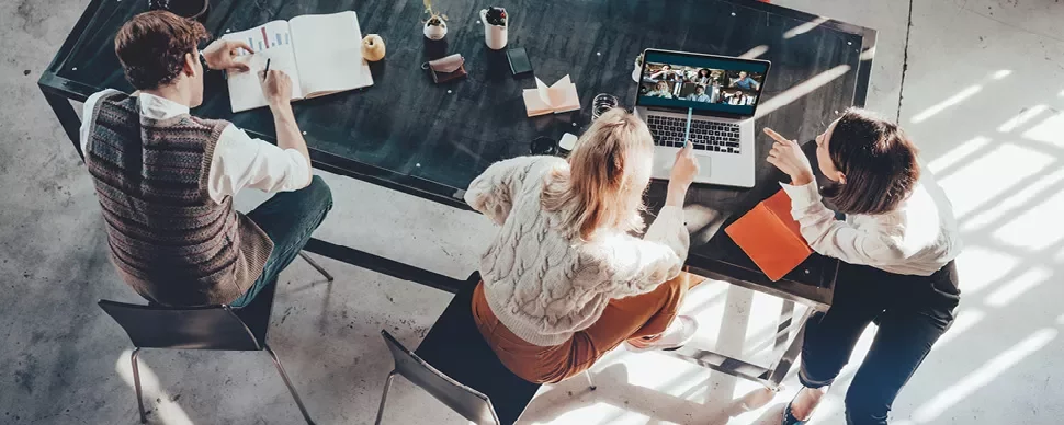 Three people working at a table with a laptop in a casual setting.
