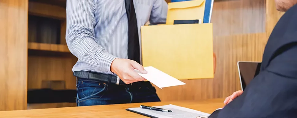 Person at a desk receiving an envelope from someone holding a box.
