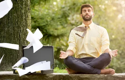Person meditating outdoors as papers fly from a briefcase.