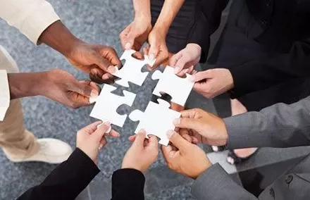 Groupe de mains assemblant des pièces de puzzle sur un fond gris.