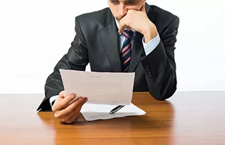 Person in suit reading a document at a desk.