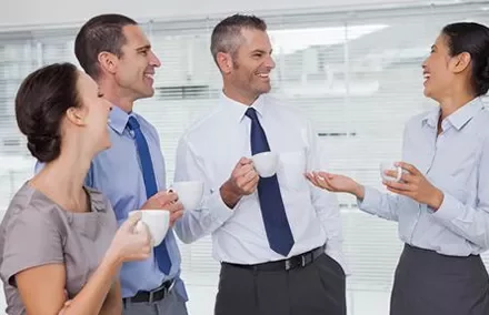 Group of people in office attire talking and drinking coffee.