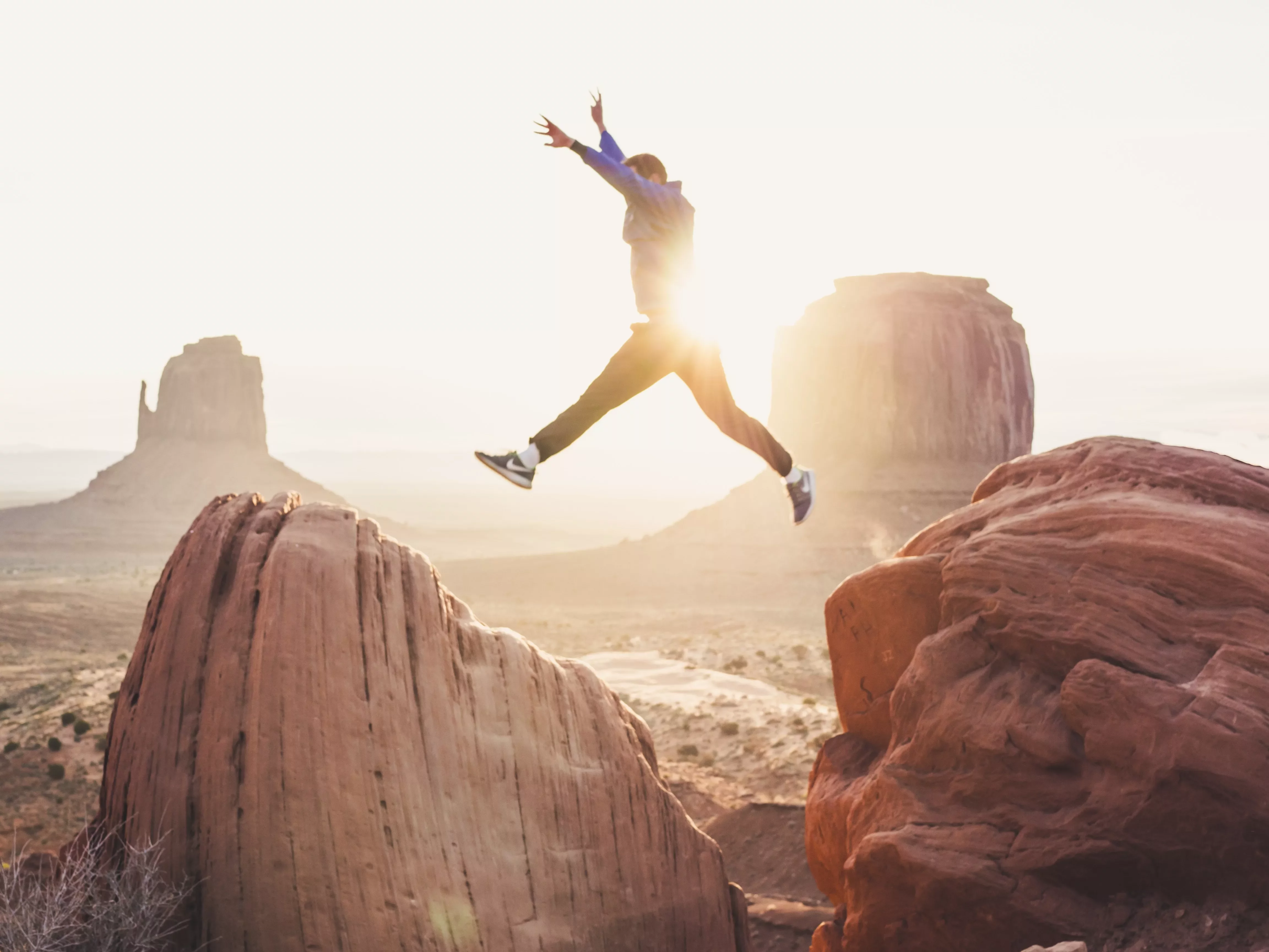 Person leaping between red rocks at sunset