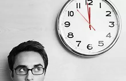 Person in glasses looking up at a wall clock.