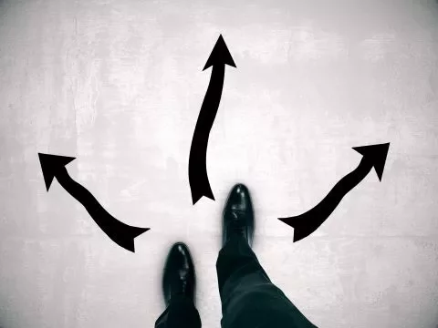 Person standing at crossroads with arrows in different directions.