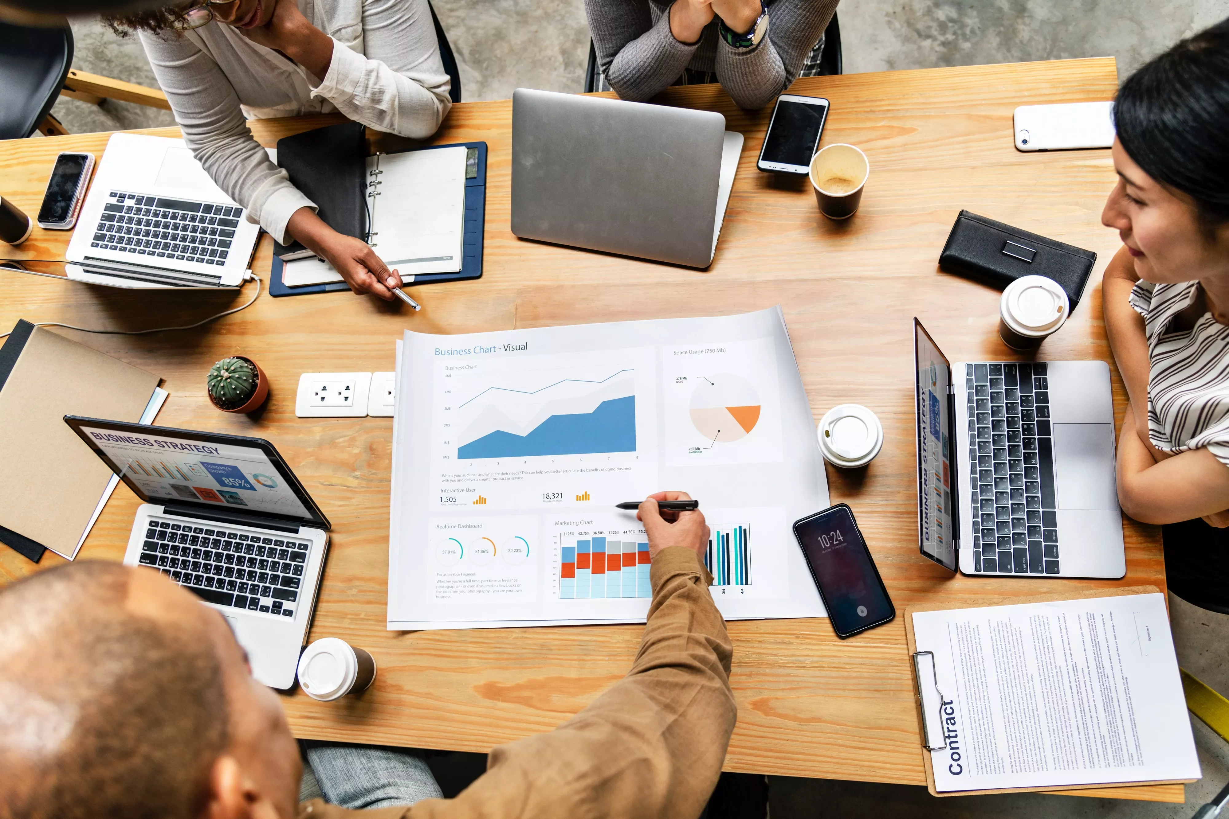 Mensen bespreken grafieken en data aan een vergadertafel met laptops.