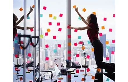 Person placing sticky notes on a high-rise office window with a city view.