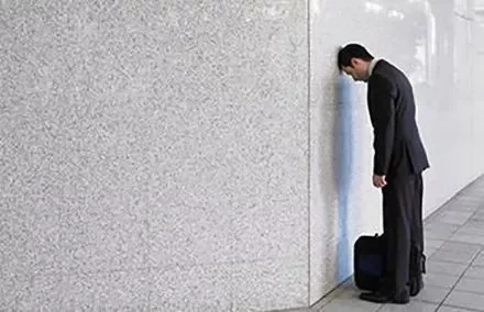 Person in a suit leaning head against a wall.